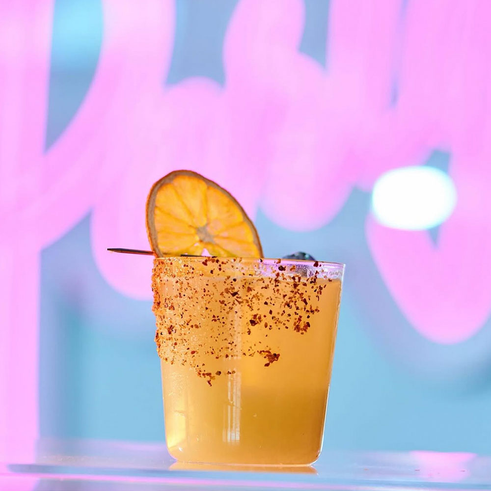 Yellow drink with tajin rim and orange garnish